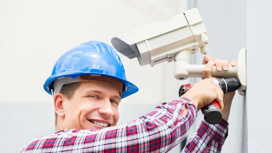 Técnico instalando uma câmera de segurança na parede externa de um imóvel