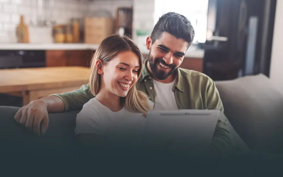 Casal sorrindo em casa olhando o notebook